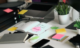 Desk with laptop, checklists and sticky notes, representing ISO 9001 clauses explained